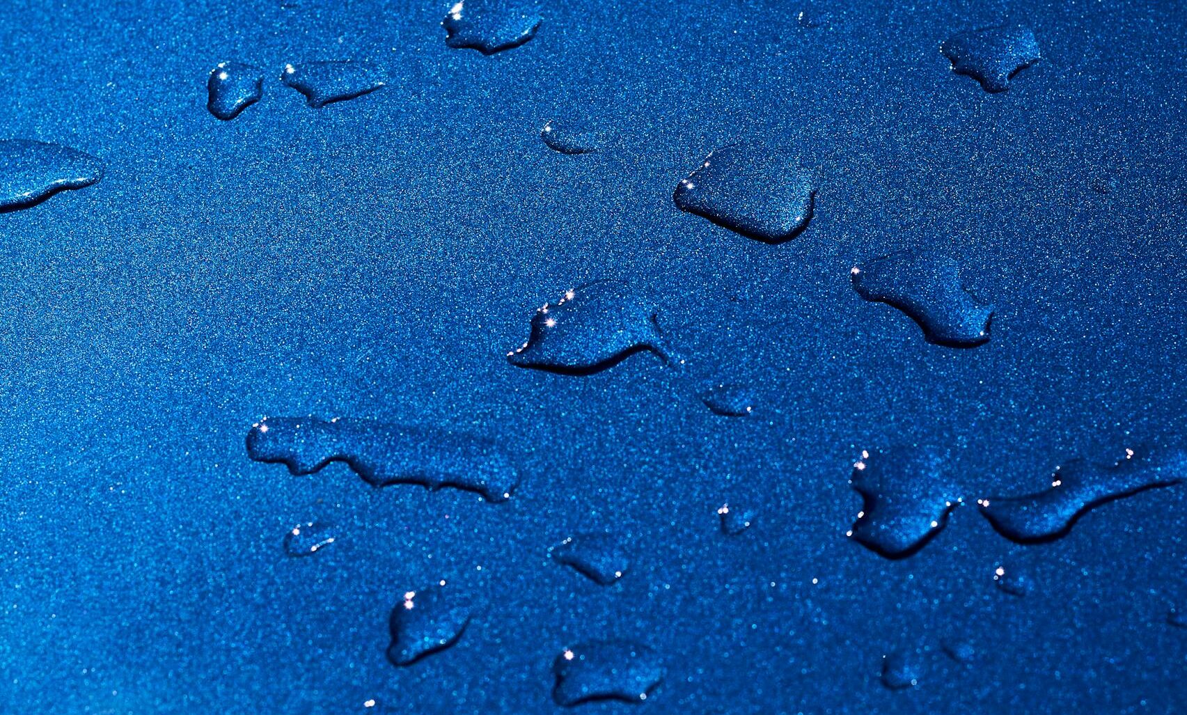 Detailed view of water droplets on a shimmering blue surface with a dark background.